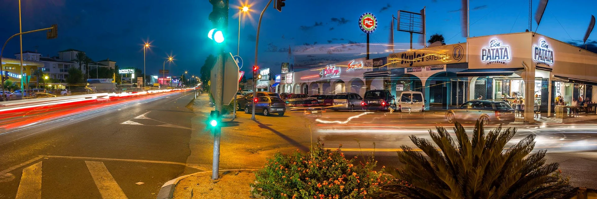 Bon Patata junto a la calle al anochecer, con letreros iluminados y estelas de luces del tráfico