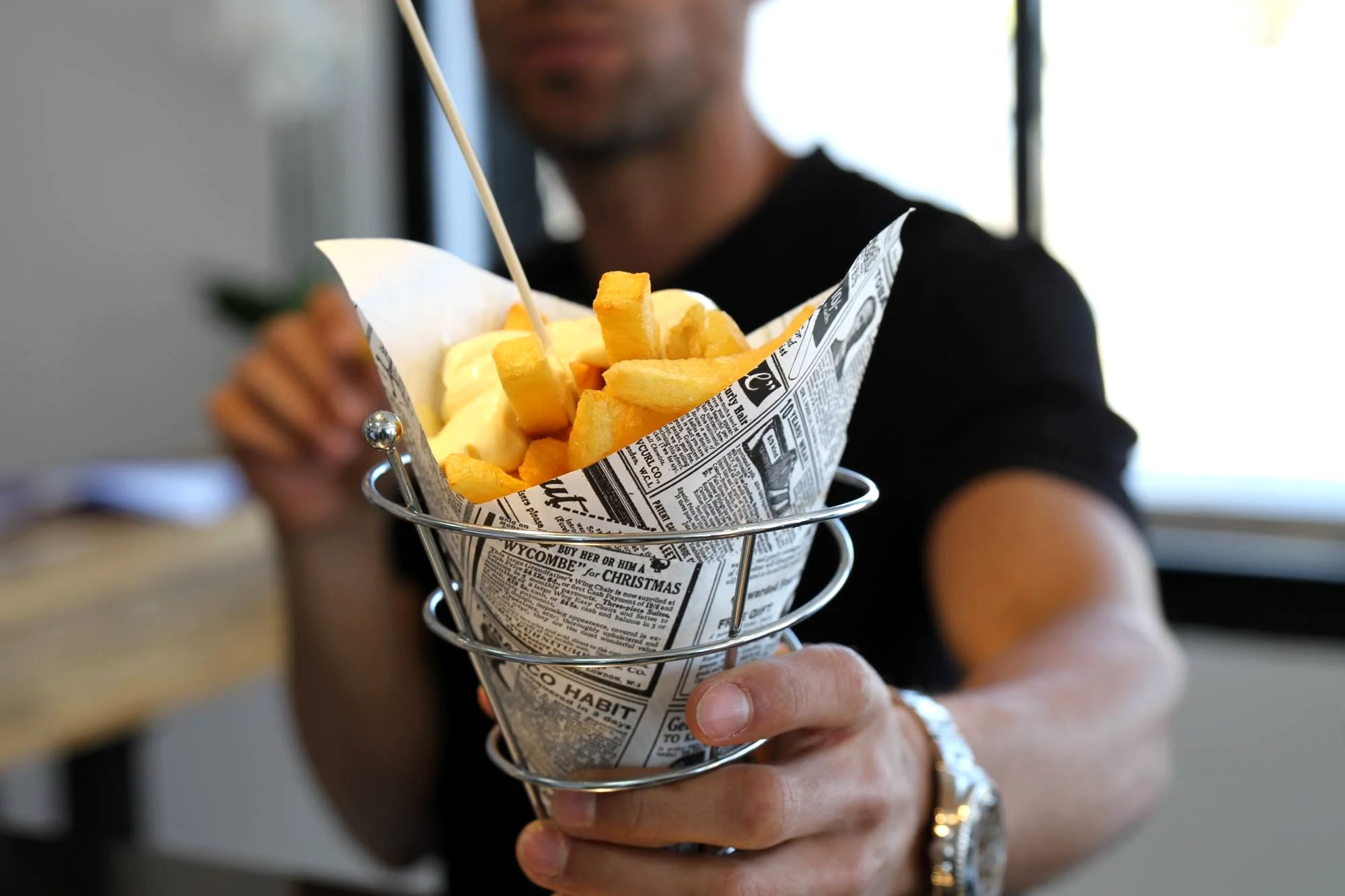 Un cucurucho de patatas fritas con mayonesa en un soporte metálico, servido en Bon Patata